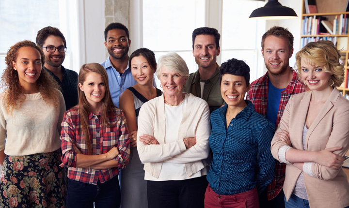 A diverse group of people standing in an office setting smiling