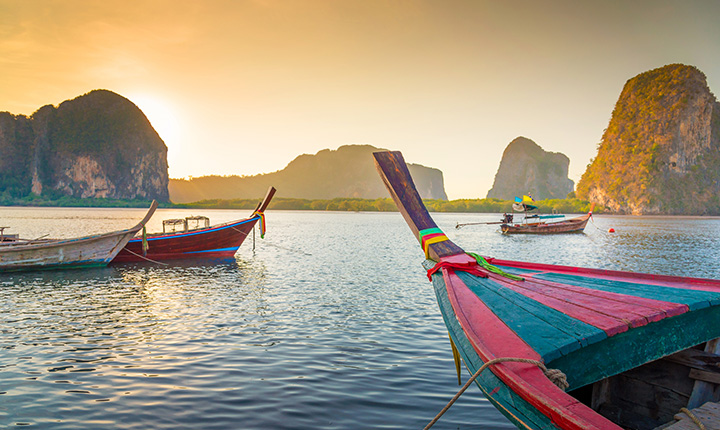 four colourful row boats sitting on the water with mountains and a sunset behind them
