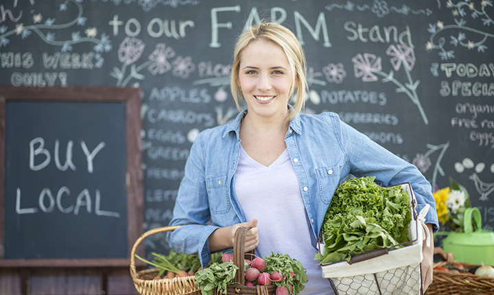 woman holding baskets of produce in front of chalk boards at farmers' market