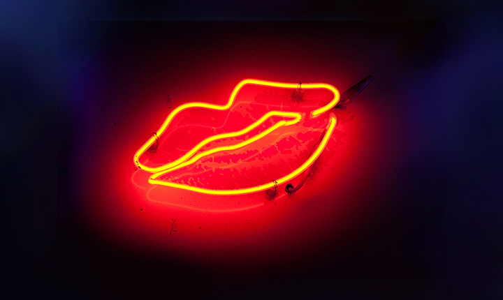 Red neon lights in the shape of lips glowing in front of a black background