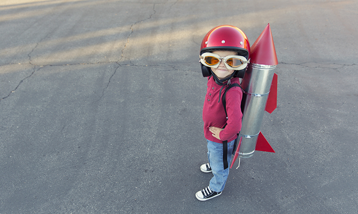 Little boy wearing big red helmet and space goggles with homemade rocket on back