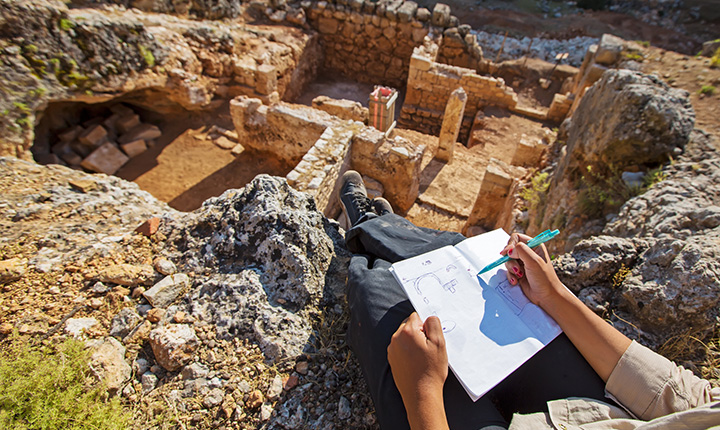 Someone sitting above some ancient ruins and sketching them
