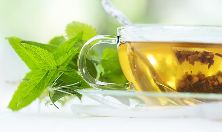 A cup of tea with mint leaves sitting beside the mug