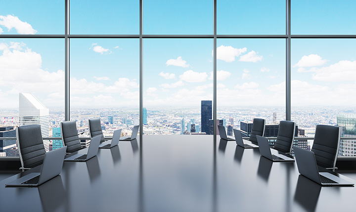 Large boardroom table equipped with laptops with panoramic city view in background