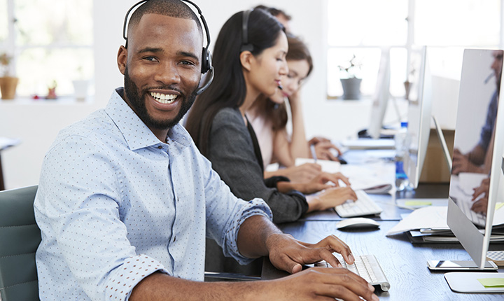 A diverse group of people at a call center smiling and answering phone calls.
