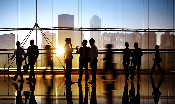 Silhouetted business people standing in front of a window with a sunset and a city scape in the background
