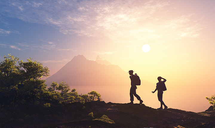 Outline of two individuals hiking in the mountains with the sun behind them