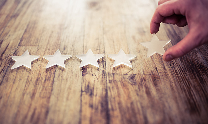 A hand placing a fifth star of a rating on a wooden background