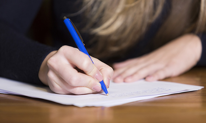 Person writing with a pen on paper at a wooden table