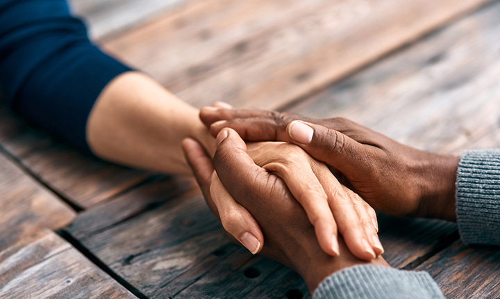 Two hands clasped together on a dark wood table. 