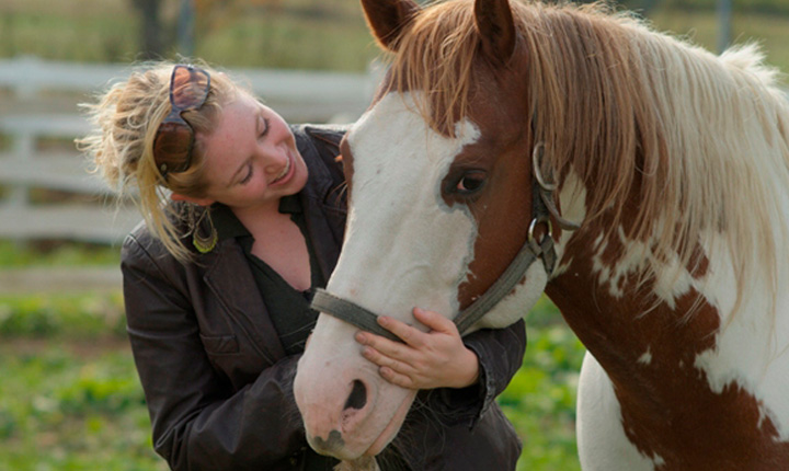 Blonde woman smiling at white and brown (paint) horse