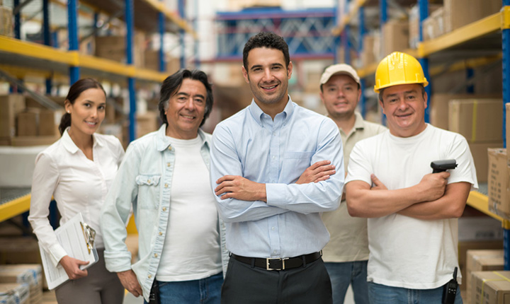 A group of workers smiling and standing in a warehouse 