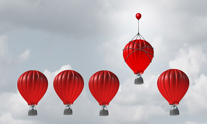 five red hot hair balloons floating in grey sky. one balloon higher than the rest. 