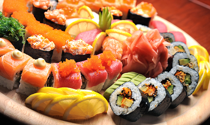 Plate of a variety of sushi, maki rolls and sashimi with lemon garnish