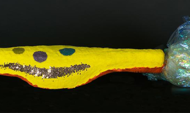 A rock painted yellow with painted eyes and a glitter mouth