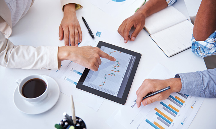 3 people analyzing charts and graphs on a tablet